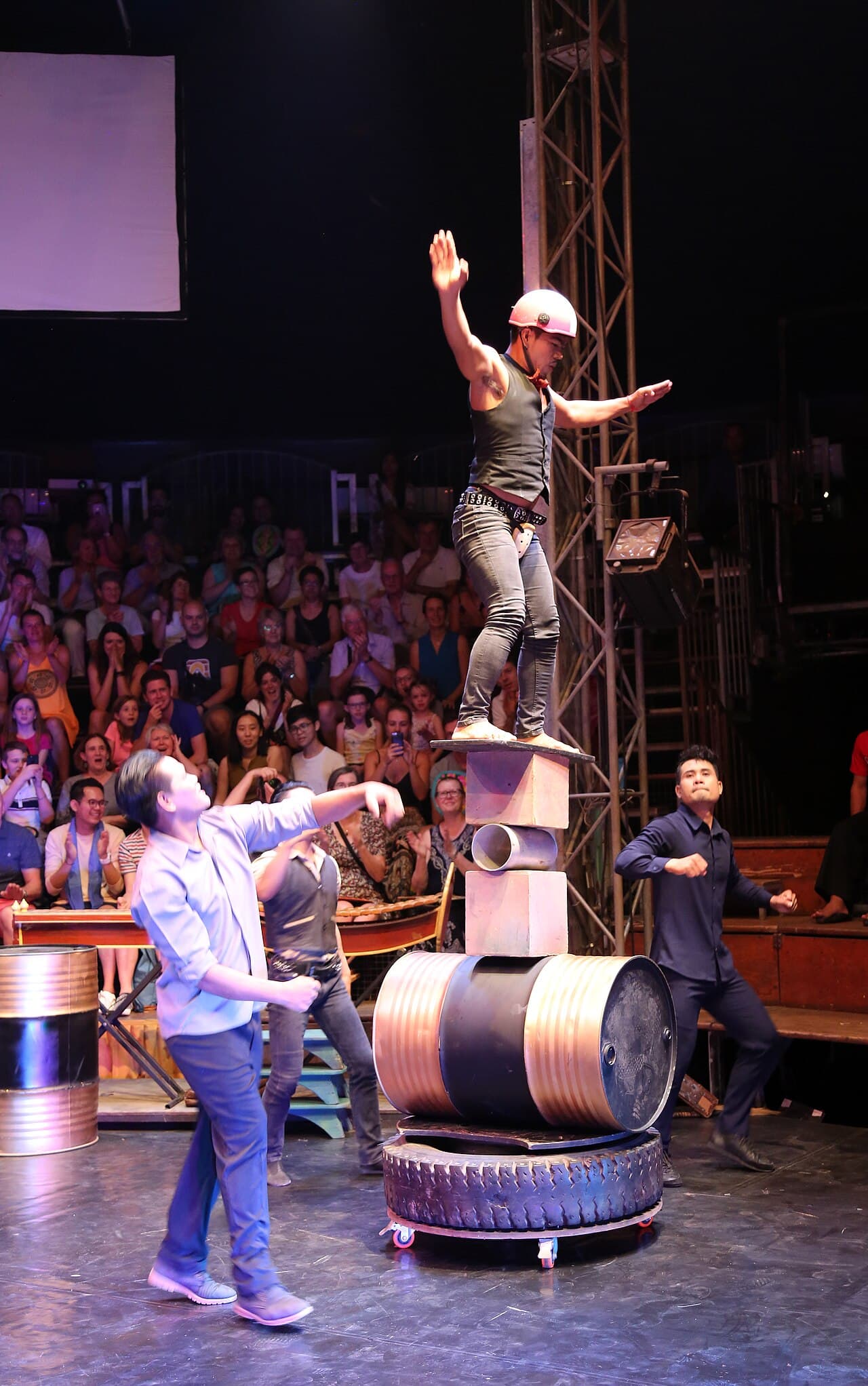 A Phare performer balancing on stacked blocks and an oil drum in front of a full audience.